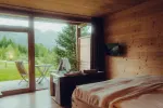 Interior of a cozy wooden room with a view of mountains and greenery outside.