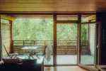 Wooden balcony with table and chairs, view of greenery.