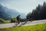 Two cyclists riding on a dirt path in a mountain landscape