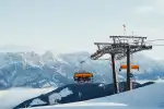 Chairlift with yellow gondolas, mountains in the background, snow on the ground