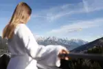 Frau im Morgenmantel mit Blick auf Berge und Himmel