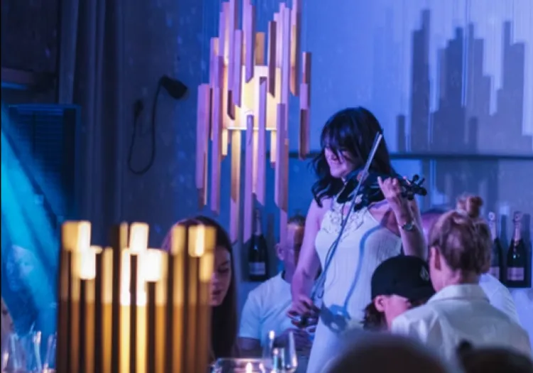 A woman playing the violin in a stylish setting with illuminated decor.