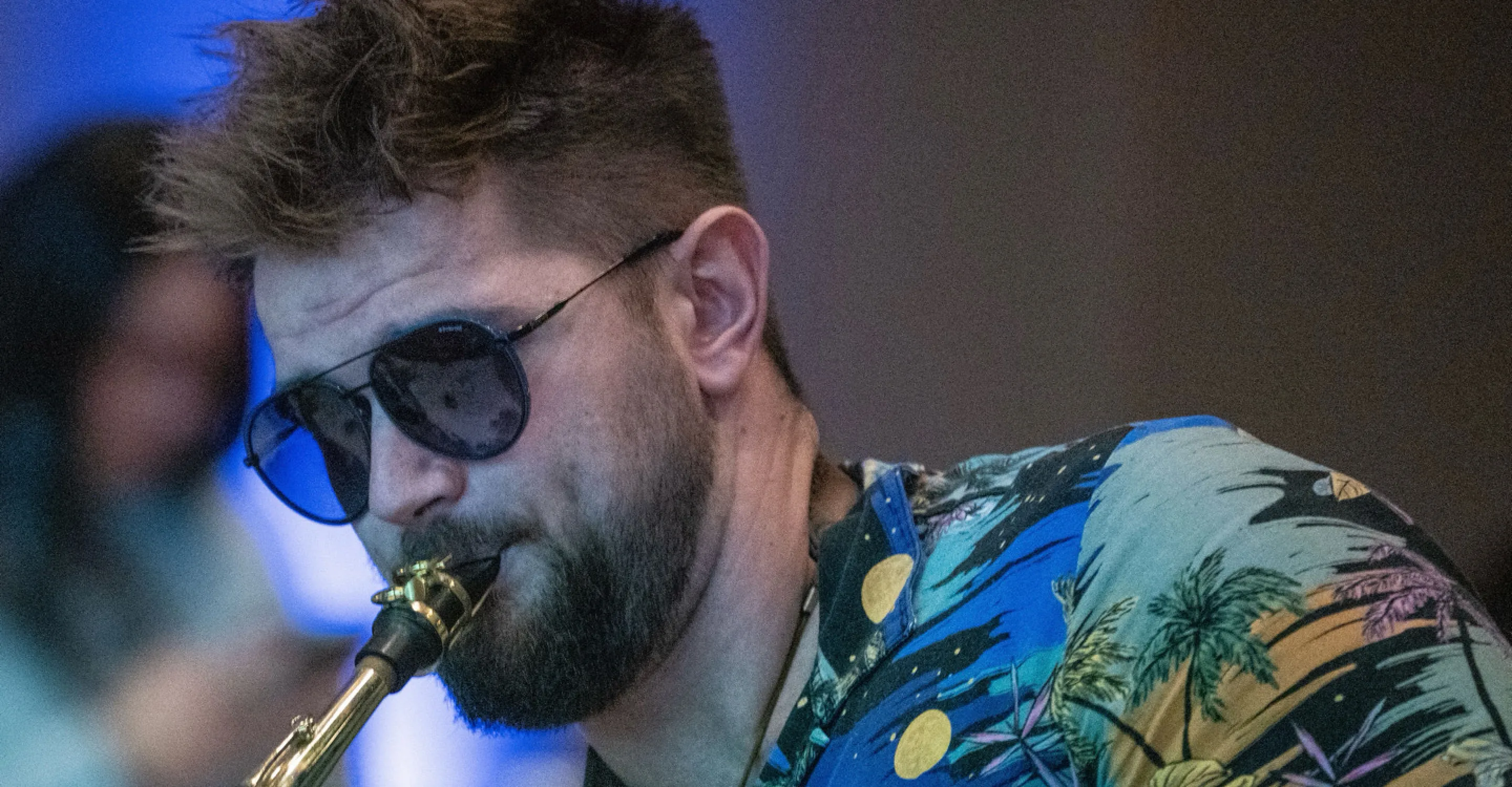 Man in sunglasses playing saxophone, colorful shirt