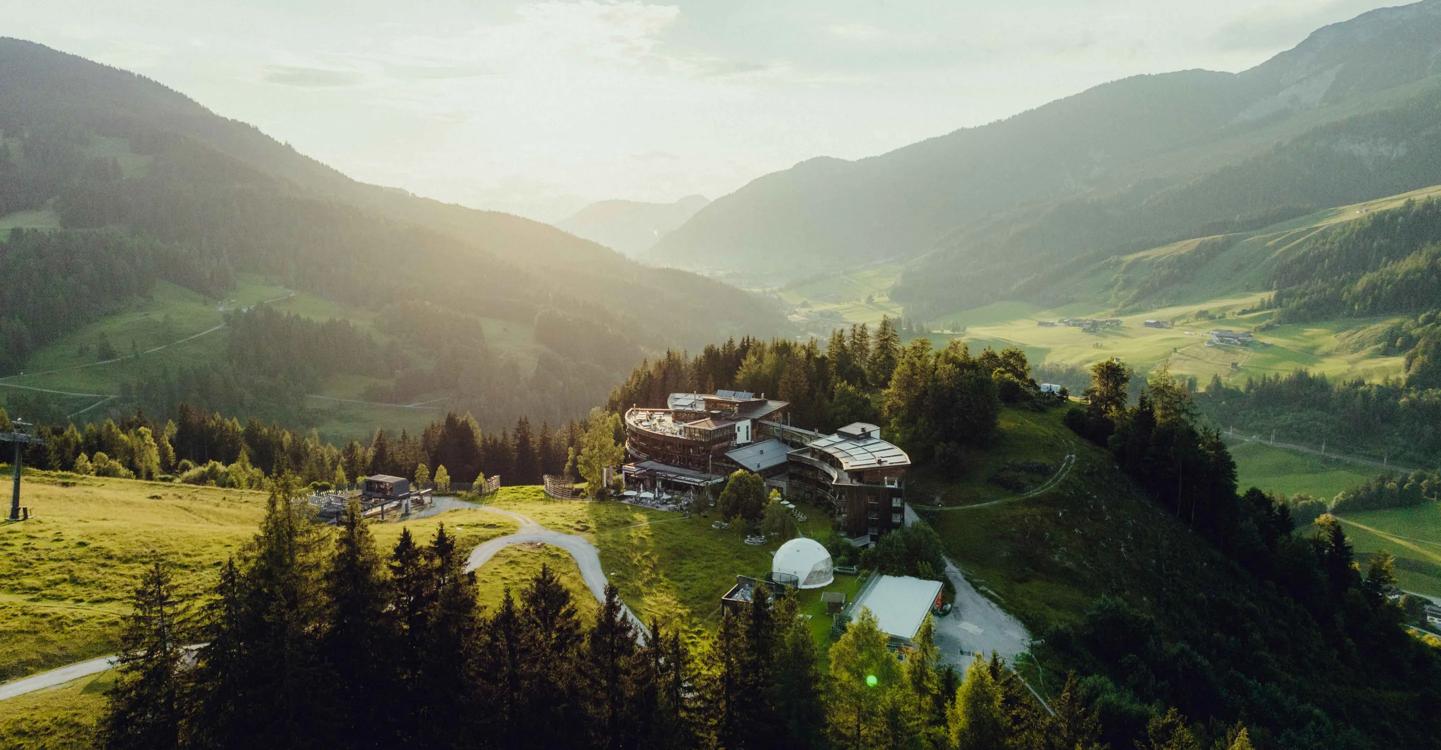 Aerial view of a mountain landscape with a modern building and green fields.