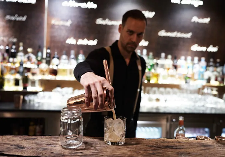 Barkeeper schöpft Cocktail in ein Glas an der Bar